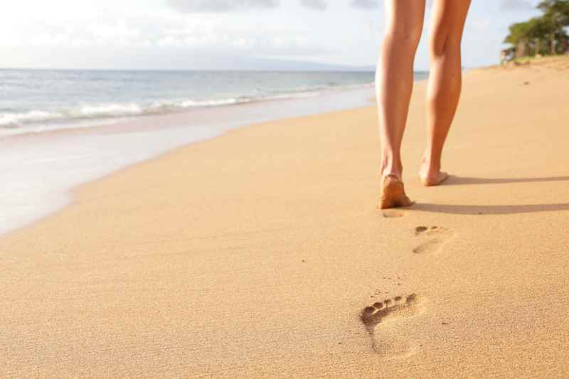 Person walking barefoot on sandy beach leaving footprints